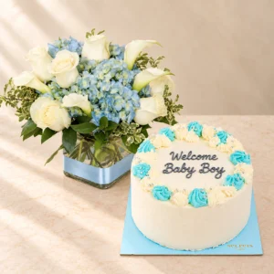 Pale blue hydrangea and white roses in a square vase beside a blue cake reading Welcome Baby Boy