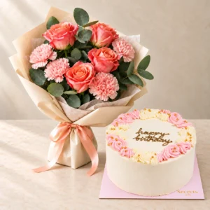 Coral-pink roses and pink carnations in peach wrapping beside a pink and ivory Happy Birthday cake